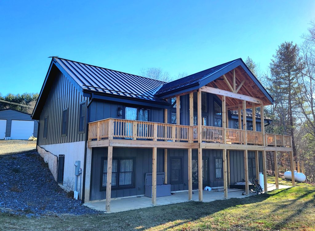 20241206_140210 Angled view of SIP-framed mountain residence with two-story walkout basement and elevated wood deck, designed for hillside terrain
