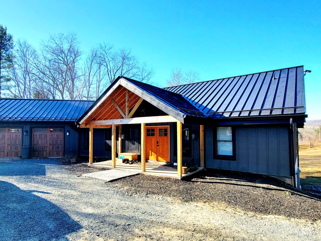 20241206_140527 Front entry of SIP-constructed mountain home featuring timber porch framing and dark vertical siding, designed for energy efficiency and durability